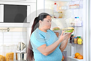 Sad overweight woman taking sandwich from refrigerator