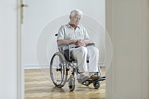 Sad paralyzed senior man in the wheelchair sitting alone at home