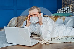 Sad patient holding hands over his head and lying on the floor at home with laptop because of coronavirus epidemy. Portrait of