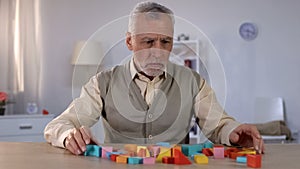 Sad pensioner looking at color building blocks on table, rehabilitation center