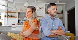 Sad pensive couple thinking of relationships problems sitting on sofa, conflicts in marriage.