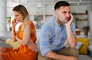 Sad pensive couple thinking of relationships problems sitting on sofa, conflicts in marriage.