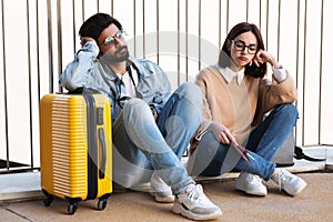 Sad pensive despaired young diverse couple in casual and glasses with passport, tickets and suitcase think