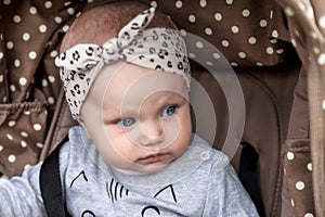 Sad pensive emotional eight-month-old blue-eyes girl sitting in stroller looking away and wait for parent