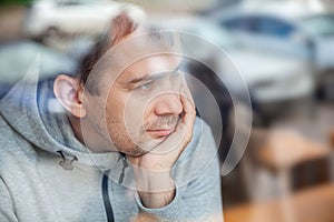 Sad pensive handsome man leaning head on hand in cafe, looking through a window