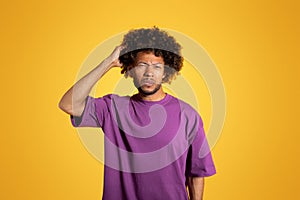 Sad pensive mature black curly guy in purple t-shirt thinking and scratching head