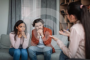 Sad pensive young caucasian man and black female listened to psychiatrist in clinic interior