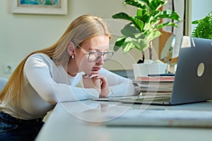 Sad pensive young teenage girl sitting near smartphone laptop at home.