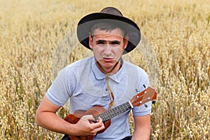 Sad person. Young beautiful caucasian man playing ukulele outside. Handsome hipster guy plays ukulele guitar on nature