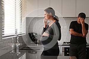 Sad pregnant woman and husband contemplating in kitchen