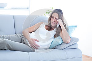 Sad pregnant woman lying on sofa