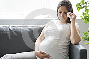 Sad pregnant woman lying on sofa at home