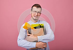 Sad pretty crying guy with a cardboard box with pens, paper airplane and different things