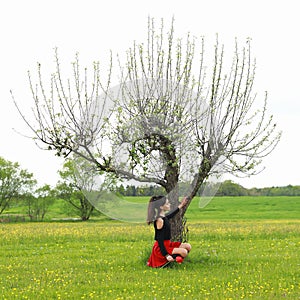 Sad pretty young teen girl with red tulip by tree