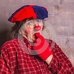 Sad and puzzled clown in glasses with red nose and glovesÐ± facial expression