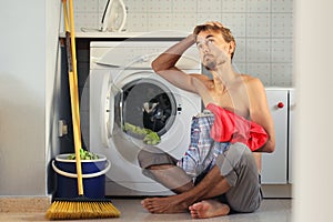 Sad, puzzled look man loads the laundry into the washing machine. Male housewife, bachelor concept