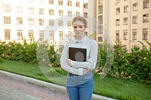 A sad red-haired girl with freckles on her face holds a folder in her hands.