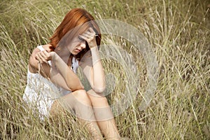 Sad red-haired girl at grass.