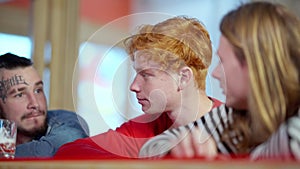 Sad redhead young man sitting with friends at bar counter talking and shaking head in slow motion. Mates supporting