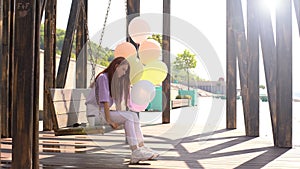 Sad redhead young woman swaying on swing holding hands large fountain of colorful balloons.