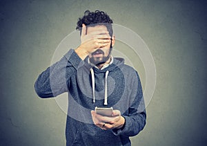 Sad regretful young man with mobile phone