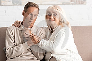 sad retired woman hugging husband with mental illness at home.