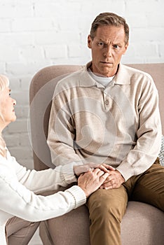 sad retired woman touching hands husband with mental illness.