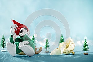 Sad Santas Helper Elf Sitting on Sledge Looking At Broken Christmas Bauble. North Pole Christmas Scene. Santas Workshop.