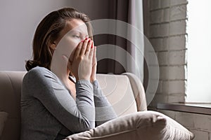Sad scared woman covering her face with hands and crying. Lonely girl sitting near window with pillow on a sofa of apartments.