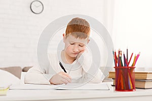 Sad schoolboy doing homework at home alone