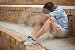 Sad schoolboy sitting alone on steps in campus