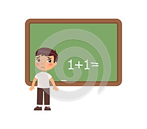 Sad schoolboy is standing in front of a blackboard. Kid cannot solve the example.