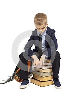 Sad schoolboy in a suit sitting on a pile of books, head bowed. Isolated on a white background.