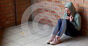 Sad schoolgirl sitting alone on floor
