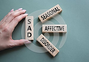 Sad - Seasonal Affective Disorder symbol. Wooden blocks with words Sad. Businessman hand. Beautiful grey green background.