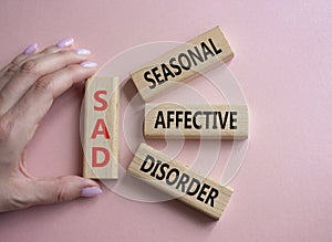 Sad - Seasonal Affective Disorder symbol. Wooden blocks with words Sad. Businessman hand. Beautiful pink background. Business and