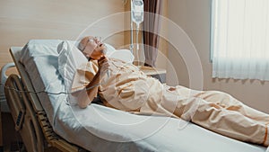 Sad senior Asia man having having heart attack lying on hospital bed and press emergency button. Sick aged guy lying hospitalized