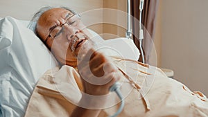 Sad senior Asia man having having heart attack lying on hospital bed and press emergency button. Sick aged guy lying hospitalized