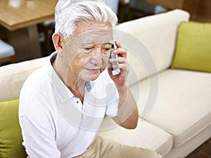 Sad senior asian man talking on cellphone