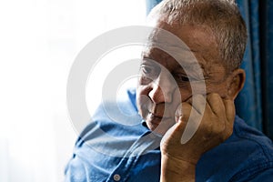 Sad senior man with hand on chin sitting by window