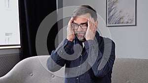 Sad senior man with headache sitting alone in a empty room