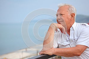 Sad senior on veranda near seacoast, looking afar photo