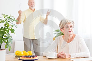 Sad senior woman arguing with her husband standing in blurred ba