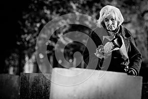 Sad Senior Woman With Flowers Standing By Grave