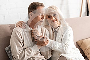 sad senior woman hugging husband with mental illness at home.