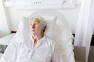 Sad senior woman lying on bed at hospital ward