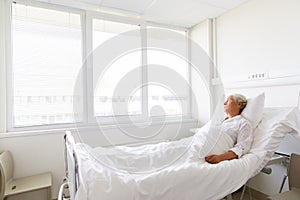 Sad senior woman lying on bed at hospital ward