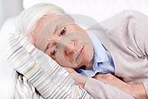 Sad senior woman lying on pillow at home