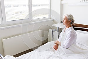 Sad senior woman sitting on bed at hospital ward