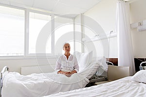 Sad senior woman sitting on bed at hospital ward